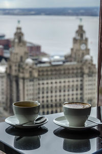 Coffee cups on table against royal liver building seen through window