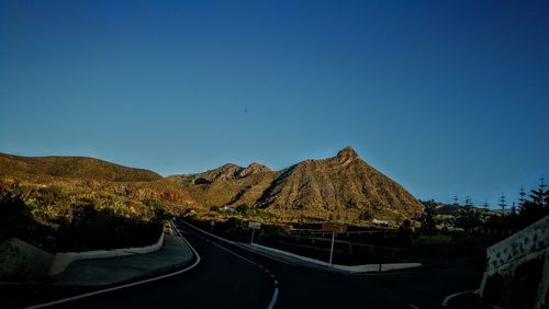 Road by mountain against clear blue sky