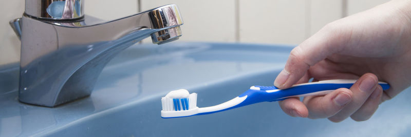 Cropped hand of woman brushing teeth at sink