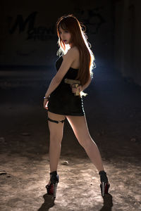 Rear view of young woman holding handgun while standing on floor