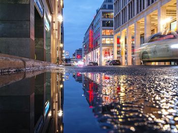Reflection of illuminated buildings in puddle on street
