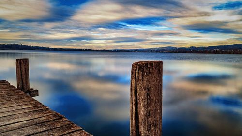 Wooden posts on pier over lake against sky