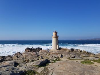 Lighthouse on rock by sea against clear sky