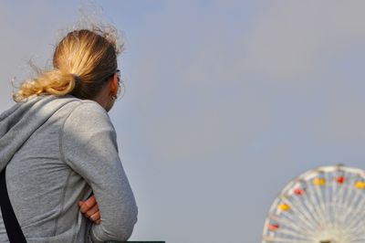 Low angle view of woman looking at ferris wheel against cloudy sky