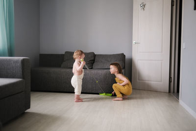 Baby 1 year old and older sister 3 years old with mop help mom clean living room with sofas