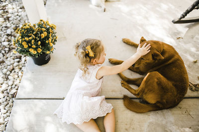 High angle view of girl petting dog while lying on porch