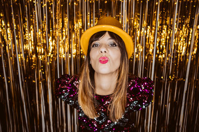 Portrait of young woman in hat blowing kiss against golden backgrounds