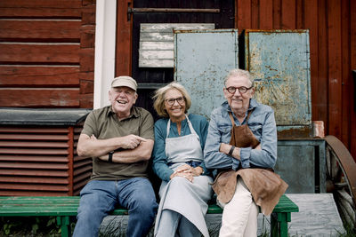 Portrait of smiling senior coworkers sitting on bench against hardware store
