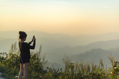 Rear view of woman photographing against sky during sunset