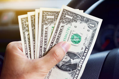 Cropped image of person holding paper currency against steering wheel of car