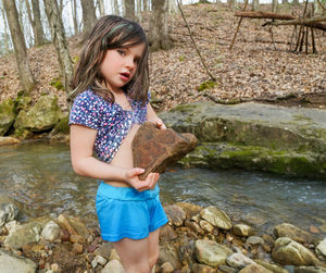 Portrait of cute girl holding rock while standing in forest