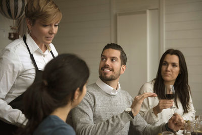 Business people talking to woman wearing apron while winetasting at table