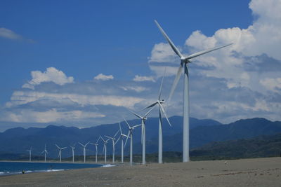 Wind turbines by beach against sky