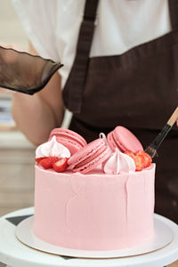 Woman pastry chef decorates pink cake with macaroons and berries, close-up. cake making process