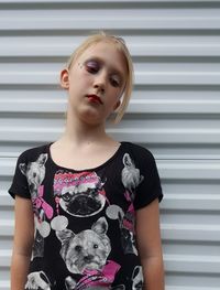 Close-up of teenage girl with make-up looking down while standing against shutter