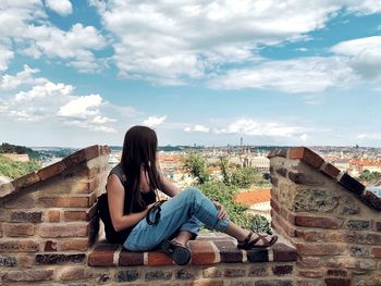 Woman sitting on wall against buildings and sky