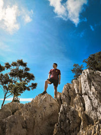 Low angle view of man standing on rock against sky