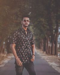 Portrait of young man wearing sunglasses standing against trees