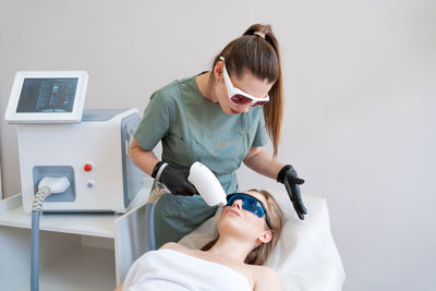 Therapist cosmetologist undergoes laser treatment on face young woman in beauty