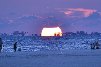 Silhouette people on beach against sky during sunset