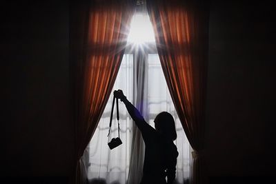 Rear view of silhouette woman holding camera at home