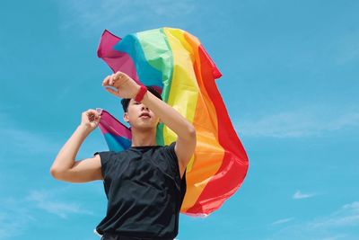 Young man waving flag on blue sky background.