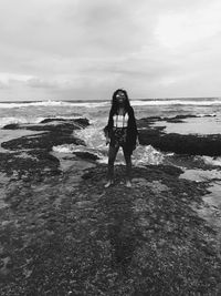 Smiling young woman standing at beach against sky