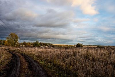 Dirt road amidst field against sky