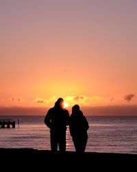 Silhouette couple standing at beach against sky during sunset