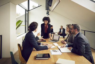 Smiling young businesswoman listening to discussion of lawyers during meeting at office