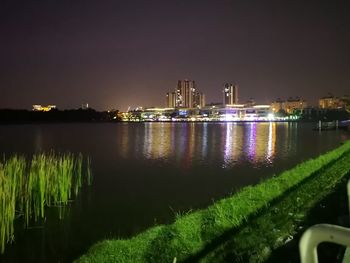 Illuminated city by river against sky at night