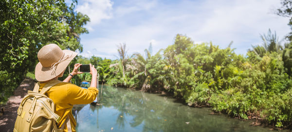 Rear view of woman wearing hat standing by lake