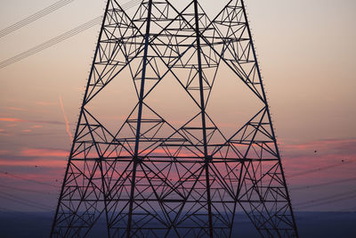 Low angle view of electricity pylon against sky during sunset