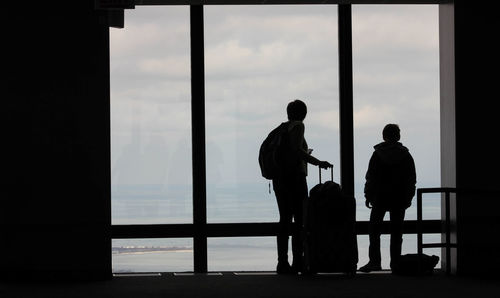 Silhouette people standing by sea against sky seen through window