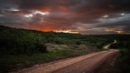 Road passing through field against cloudy sky