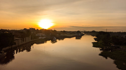 Scenic view of river by buildings against sky during sunset