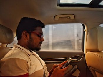 Side view of man using phone while sitting in car