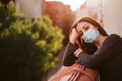 Woman wearing mask while leaning on retaining wall