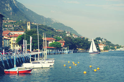 Sailboats moored in sea against buildings in city