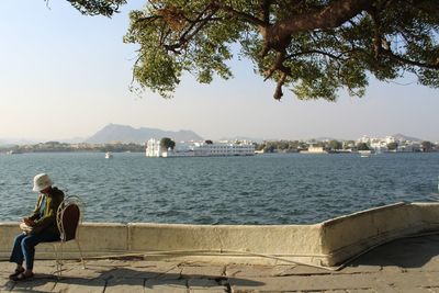 Woman sitting by sea against sky