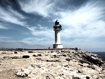 Lighthouse on rock formation against sky
