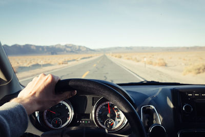 Cropped hand holding car steering wheel against clear sky