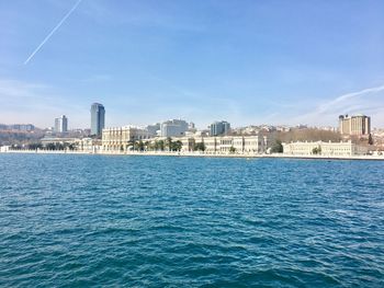 Sea by cityscape against blue sky