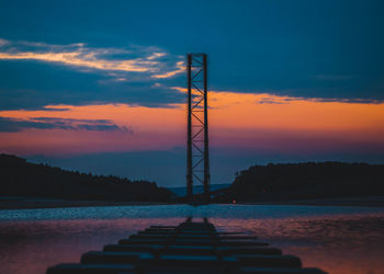 Silhouette crane by lake against sky during sunset