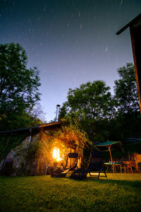 Chairs by illuminated house against starry sky at night