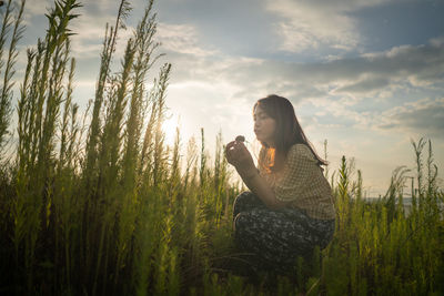 Woman sitting on field against sky during sunset