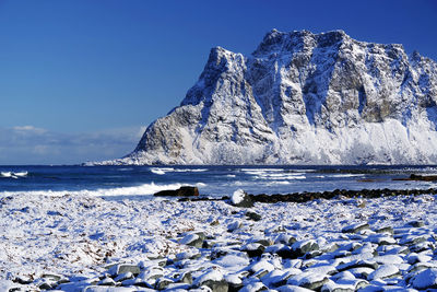 Scenic view of sea by snowcapped mountain against blue sky