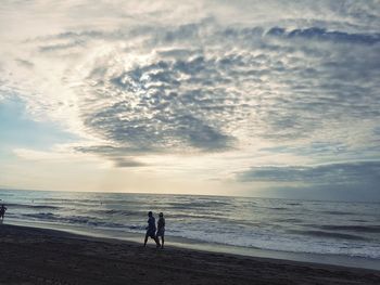 People walking on beach against sky during sunset