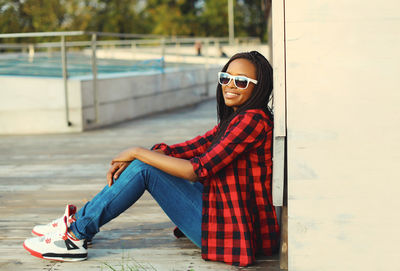 Portrait of young woman wearing sunglasses standing against wall