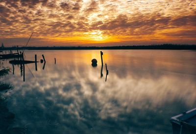 Scenic view of lake against cloudy sky at sunset
